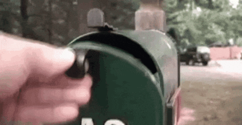 a person is opening a green mailbox with a ring on it .