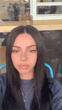 a girl with long dark hair is wearing a necklace and a blue shirt