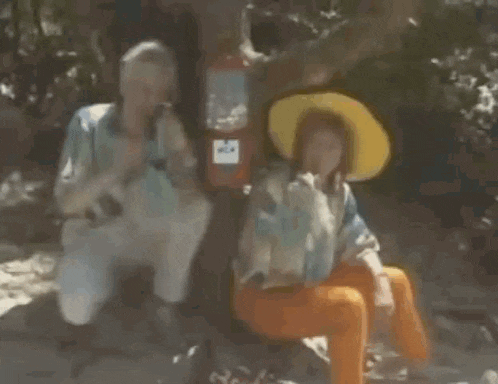 a woman in a yellow hat is sitting next to another woman in orange pants .