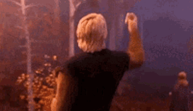 a man in a black shirt with the letter w on the back is standing in front of a forest .