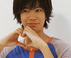 a woman in a blue and orange striped shirt is making a heart shape with her hands .