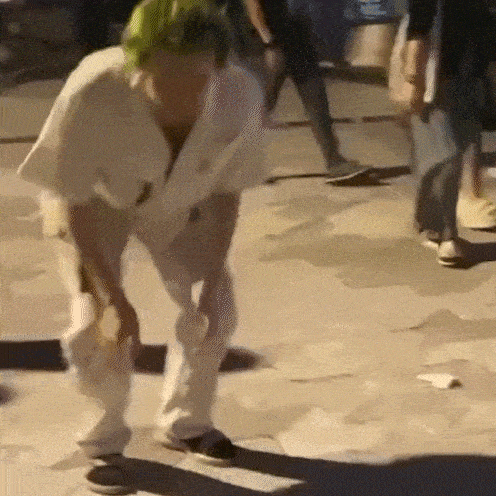 a man with green hair is standing on a sidewalk holding a bag .