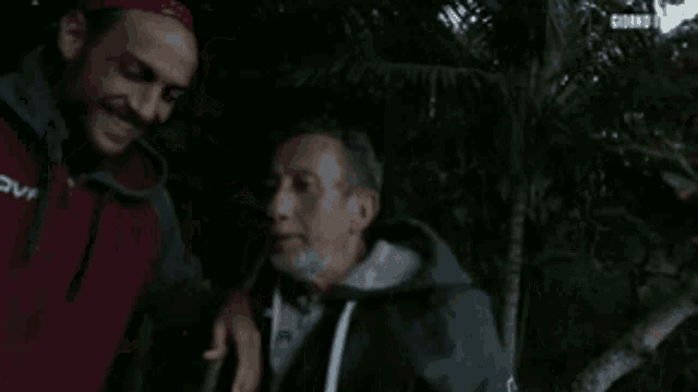 two men are standing next to each other and one of them is wearing a red jacket with the word vov on it