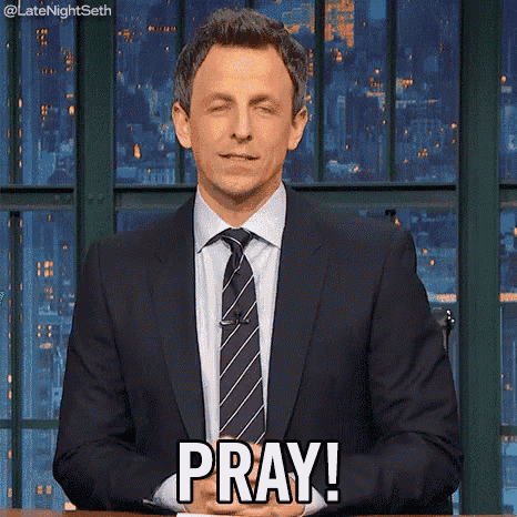 a man in a suit and tie is saying pray while sitting at a table .