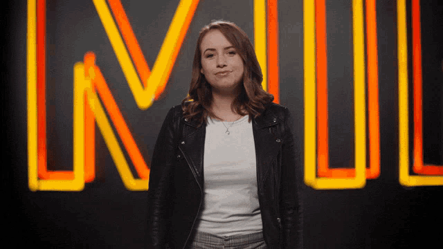 a woman in a black jacket stands in front of a neon sign that says lnw