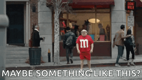 a man in a red shirt with the letter m on it is standing on a sidewalk