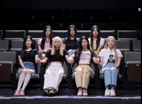 a group of girls are sitting in a theater holding hands with the letter s on the bottom right