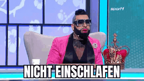 a man in a pink suit and sunglasses is sitting in a chair with a crown on his head .