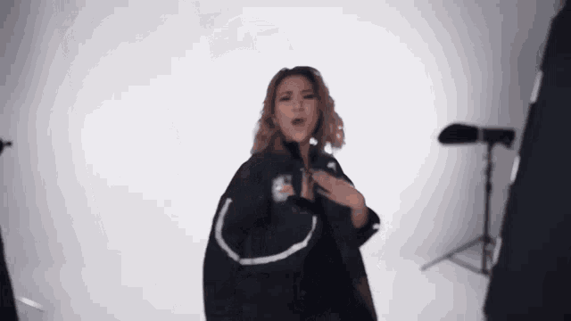 a woman in a black jacket is singing into a microphone