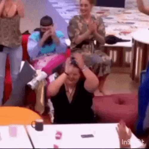 a group of people are sitting around a table with a woman covering her ears .