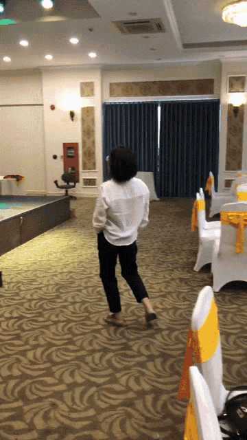 a woman in a white shirt is dancing in a room with yellow chairs