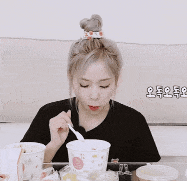 a woman in a black shirt is eating a bowl of food with a spoon in her mouth