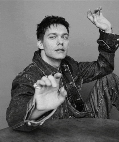 a black and white photo of a man wearing a denim jacket and overalls