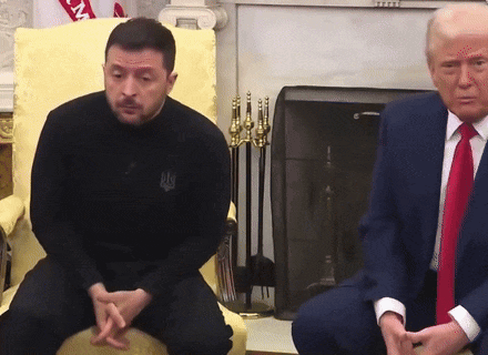 a man in a black shirt with the word ukraine on it sits next to a man in a suit