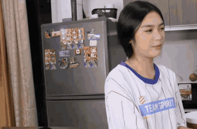 a woman wearing a shirt that says team spirit stands in front of a refrigerator