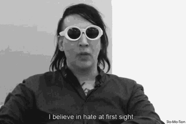 a black and white photo of a man wearing sunglasses and saying " i believe in hate at first sight "