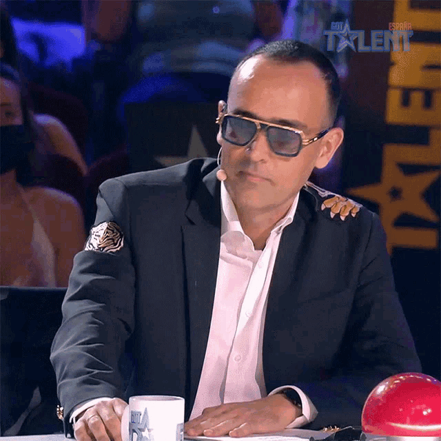 a man wearing sunglasses and a suit is sitting in front of a sign that says espana talent
