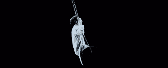 a man in a blue shirt is sitting on a swing in the dark .