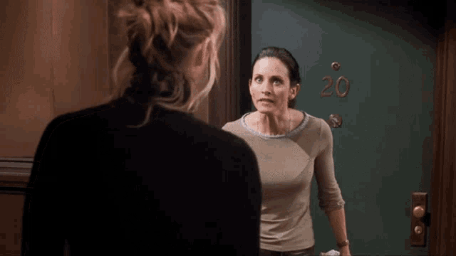 two women are standing in front of a green door that says 20
