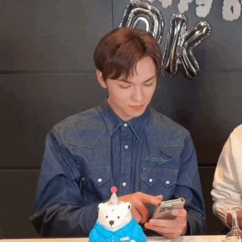 a man wearing a denim shirt that says kenzo on it looks at his phone