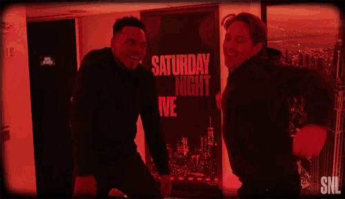 two men are standing next to each other in front of a saturday night live poster .