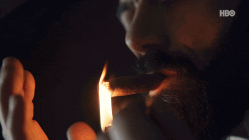 a man with a beard is lighting a cigar with a lighter with a hbo logo in the background