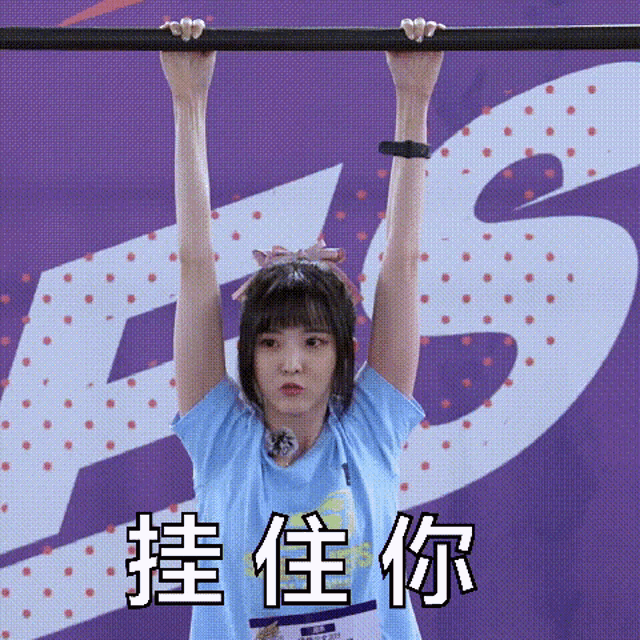 a girl is hanging upside down on a bar with chinese writing on the background .