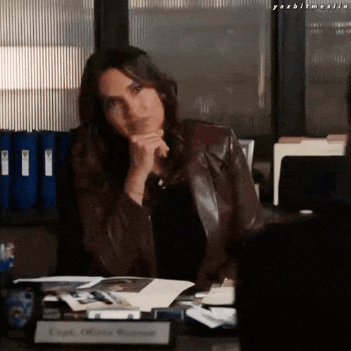 a woman in a leather jacket sits at a desk with a name tag that says captain