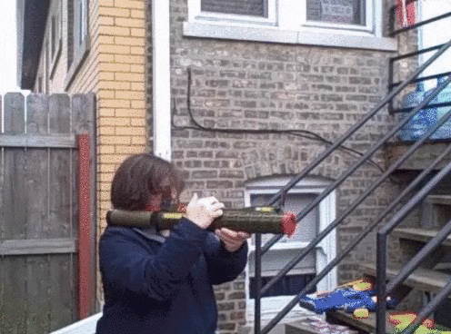 a person is holding a rocket launcher in front of a brick building