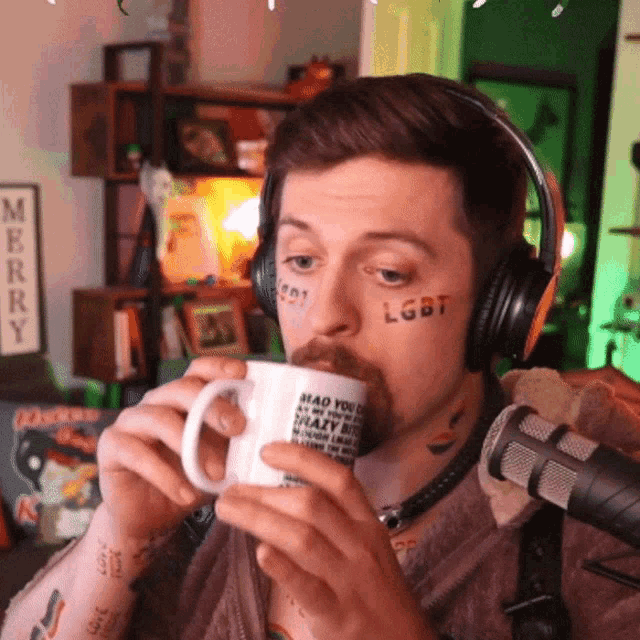 a man wearing headphones is drinking from a mug with lgbt written on his face