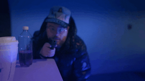 a man in a hooded jacket is pointing a gun at the camera