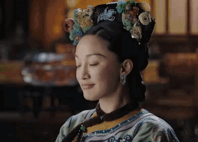 a woman wearing a crown of flowers in her hair is smiling with her eyes closed .