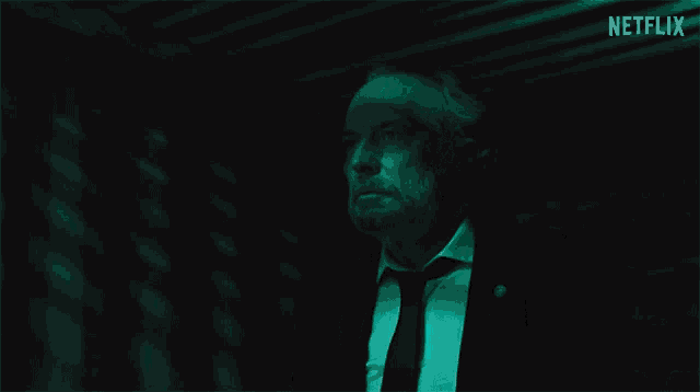 a man in a suit and tie is standing in a dark room with netflix written on the bottom