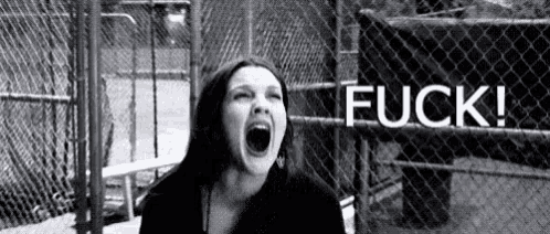 a woman is screaming in front of a chain link fence with the word fuck written in white .