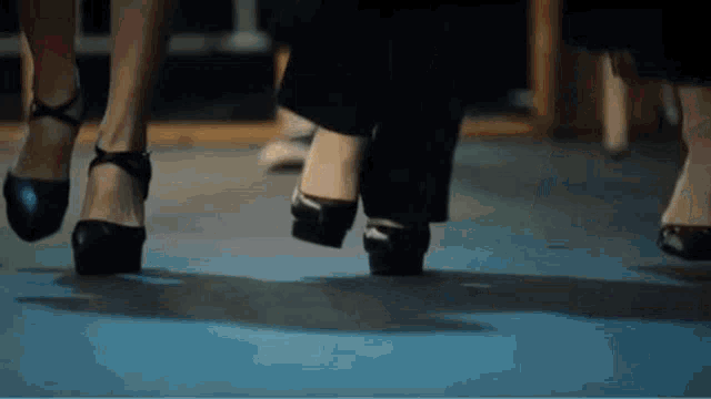 a group of women are walking on a blue carpet wearing high heels .
