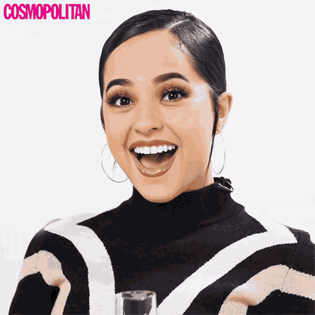 a woman in a black and white striped sweater is smiling in front of a cosmopolitan logo