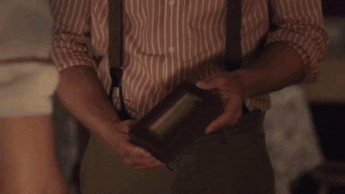 a man in a striped shirt and suspenders is holding a wooden box