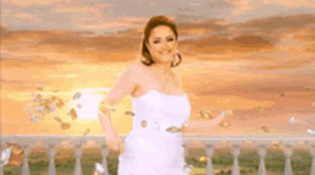 a woman in a white dress is standing on a balcony with a sunset in the background