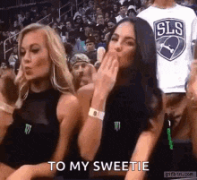 two women are sitting in a stadium and one of them is blowing a kiss .