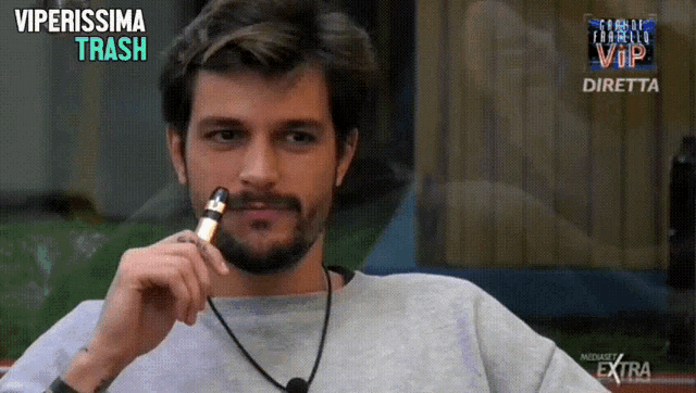 a man with a beard is smoking an electronic cigarette in front of a screen that says viperissima trash