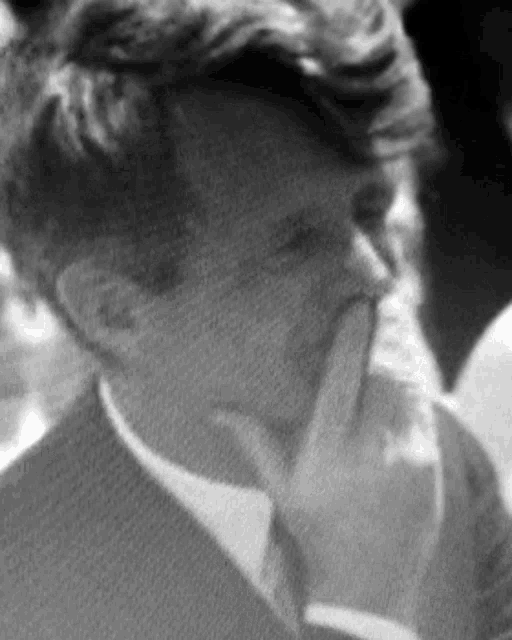 a black and white photo of a man in a suit and tie covering his mouth with his hand .