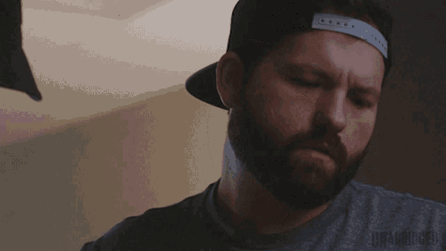 a man with a beard is wearing a hat and a gray shirt with the word unanswerable on it