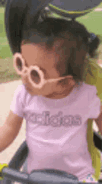 a little girl wearing sunglasses and an adidas shirt is sitting on a stroller .