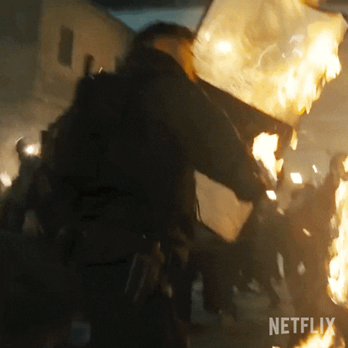 a man is standing in front of a crowd of people holding a burning flag .