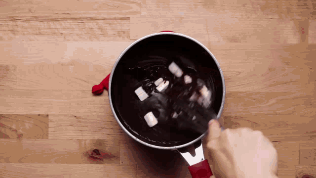 a person is stirring a pot of chocolate with marshmallows