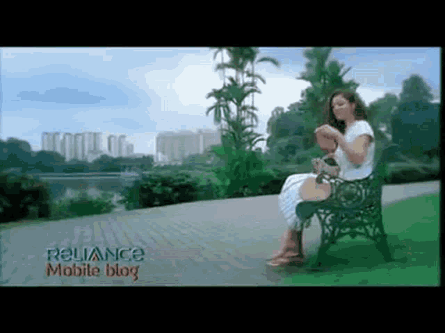 a woman is sitting on a bench in a park with a reliance mobile blog advertisement behind her