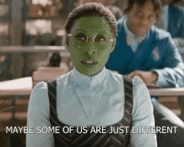 a woman wearing a green mask and glasses is sitting at a desk in a classroom .