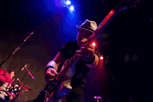 a man in a hat is playing a guitar in front of a drum set