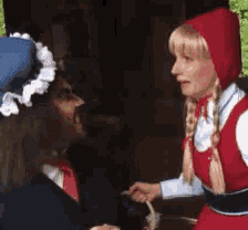 a woman in a red hooded dress is talking to a man in a blue hat .