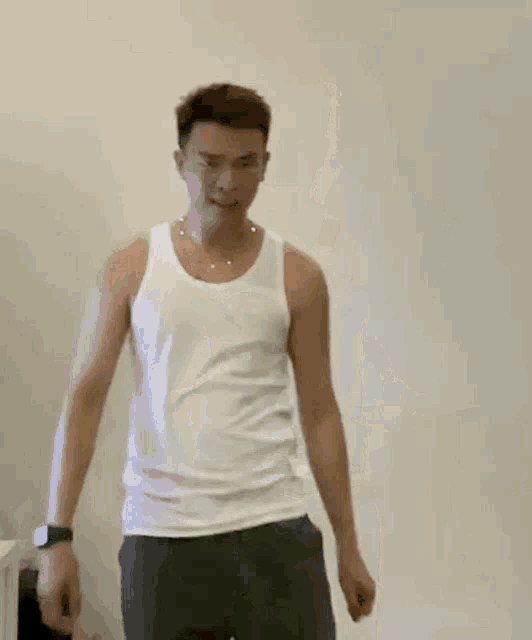 a man in a white tank top and gray pants is waving his hands in front of a white wall .